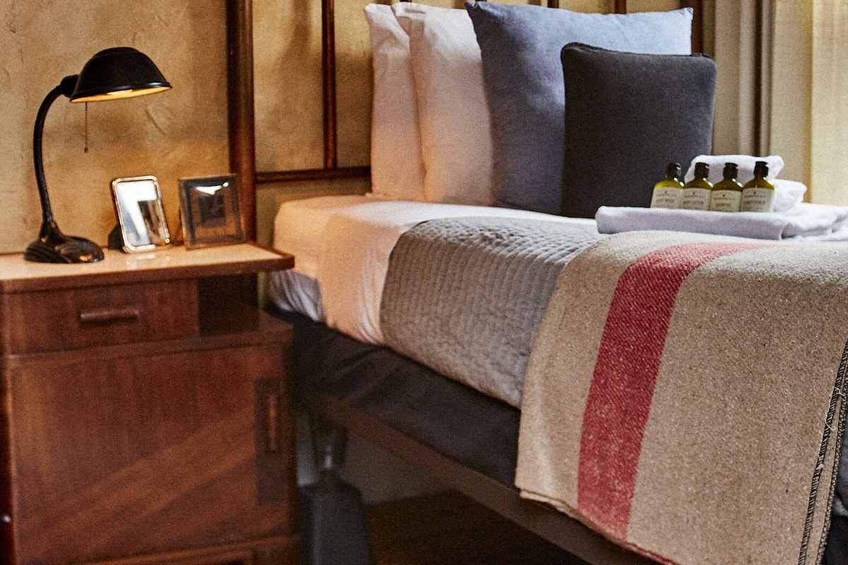 A neatly made bed with a wooden headboard, a bedside table with a lamp, and a framed picture on the wall.