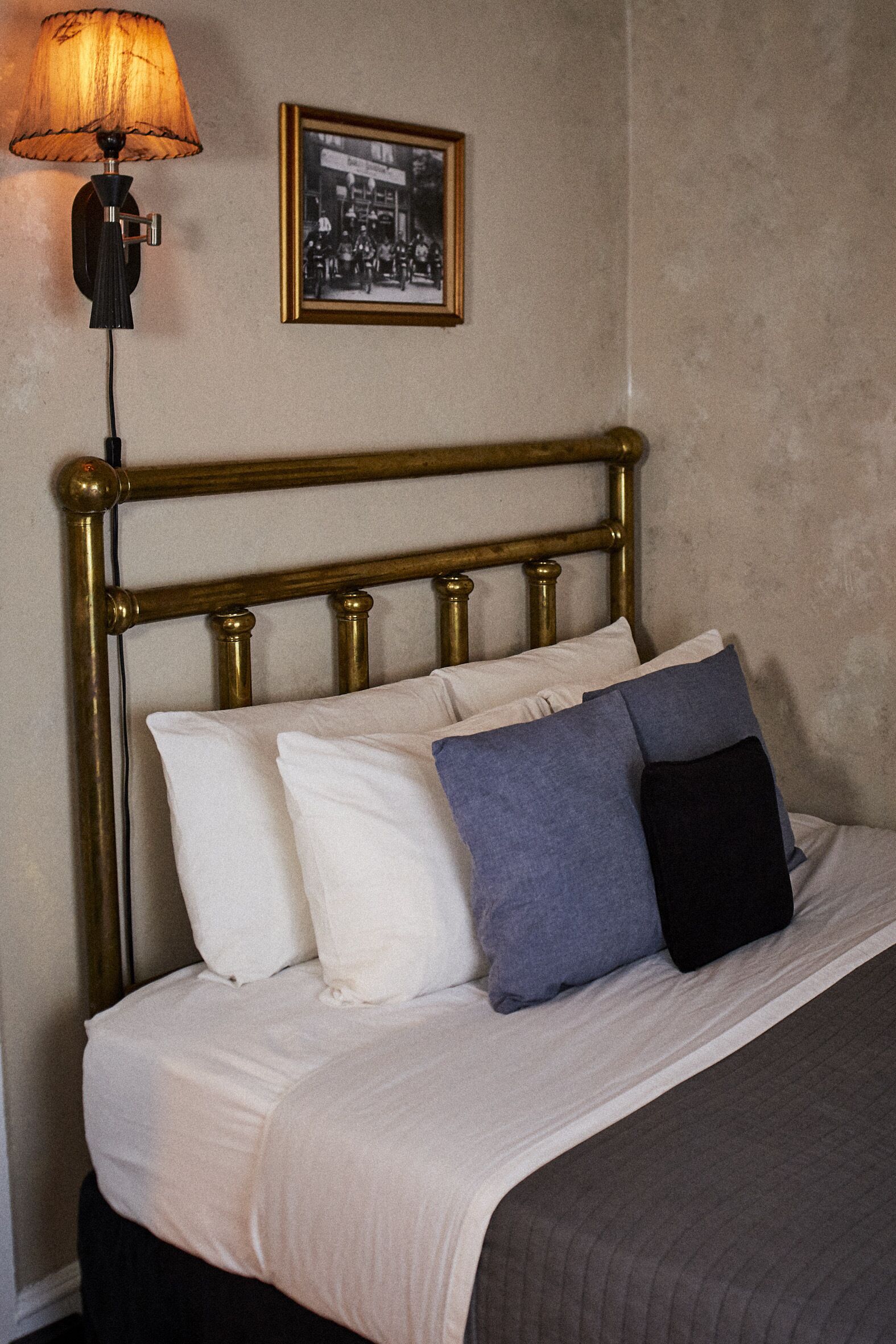 Ein Bett mit Messing-Kopfteil, weißen und blauen Kissen sowie einer Lampe auf dem Nachttisch.