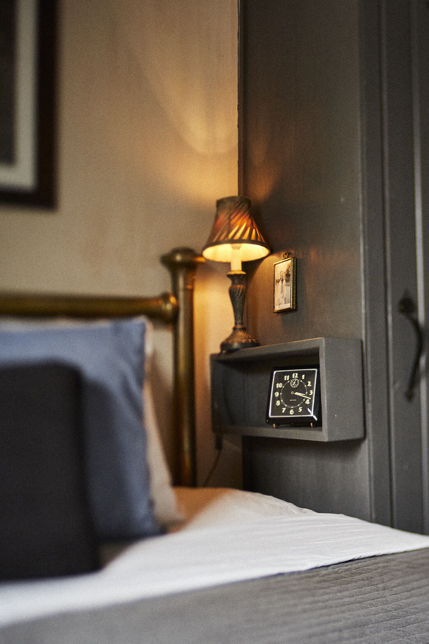 A bed with a blue pillow, a bedside lamp, and a wall-mounted clock.