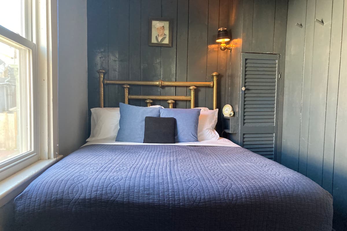 A bed with a quilted cover, a wooden headboard, and a wall-mounted clock.