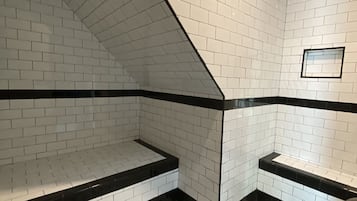 A corner of a room with white and black tiled walls and floor, featuring a black ledge and a small window.
