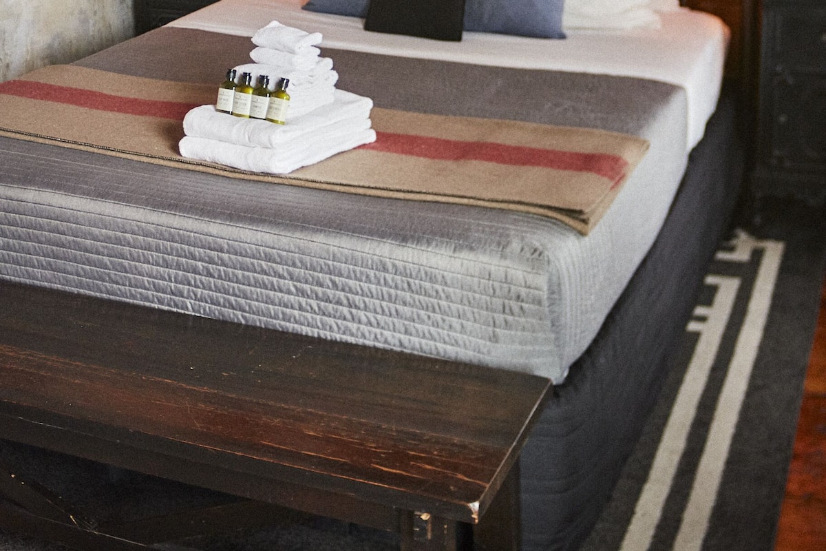 A neatly made bed with a striped blanket, pillows, and a set of towels. There are two bedside tables with lamps, and a ceiling fan above.