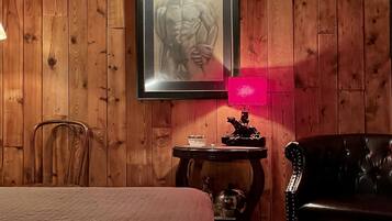 Une pièce aux murs en bois, avec un lit, un canapé en cuir noir, une petite table avec une lampe et un tableau encadré au mur.