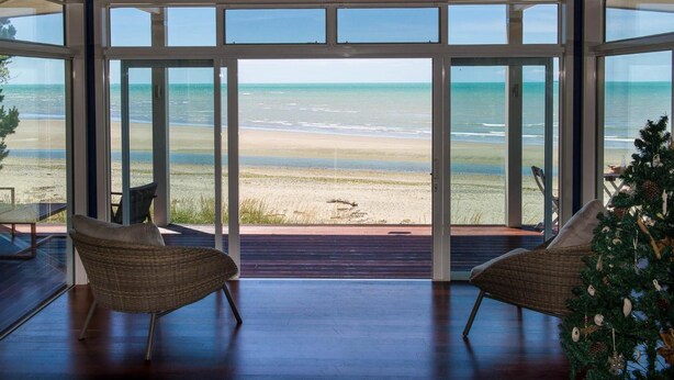 Une pièce spacieuse dotée de grandes portes vitrées donnant sur la plage, aménagée avec des fauteuils en osier et une petite table.
