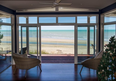 A spacious room with large glass doors leading to a beach view, furnished with wicker chairs and a small table.