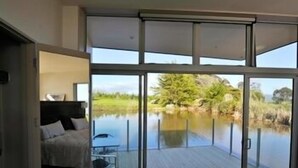 Une chambre moderne dotée d’une grande porte-fenêtre coulissante qui donne sur une terrasse offrant une vue sur un lac et la verdure environnante.