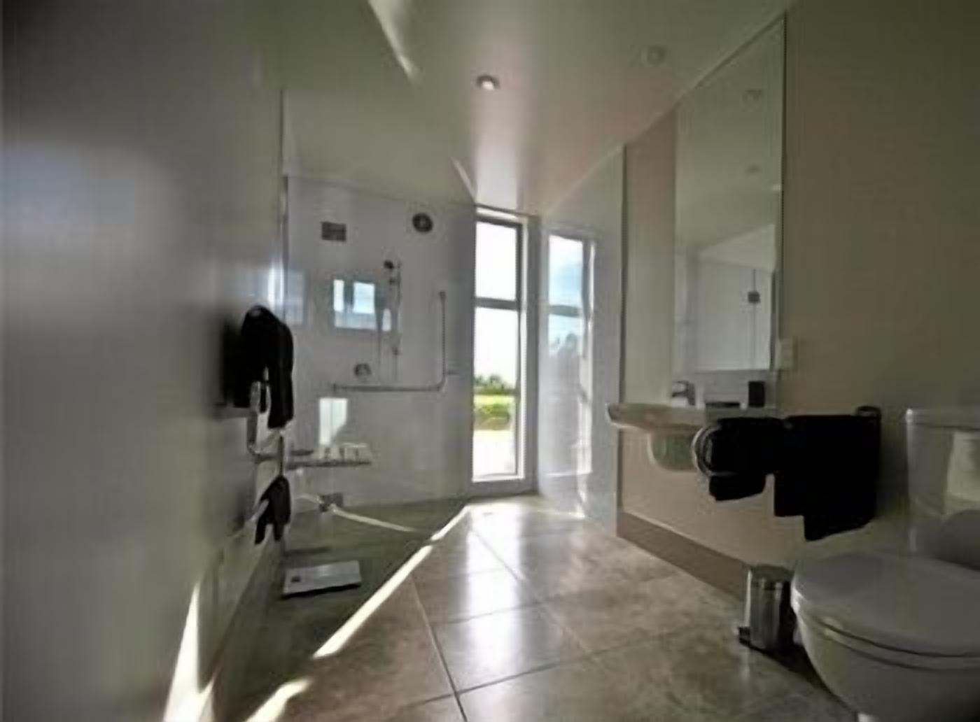 A modern bathroom with a toilet, sink, and mirror. There is a window providing natural light.