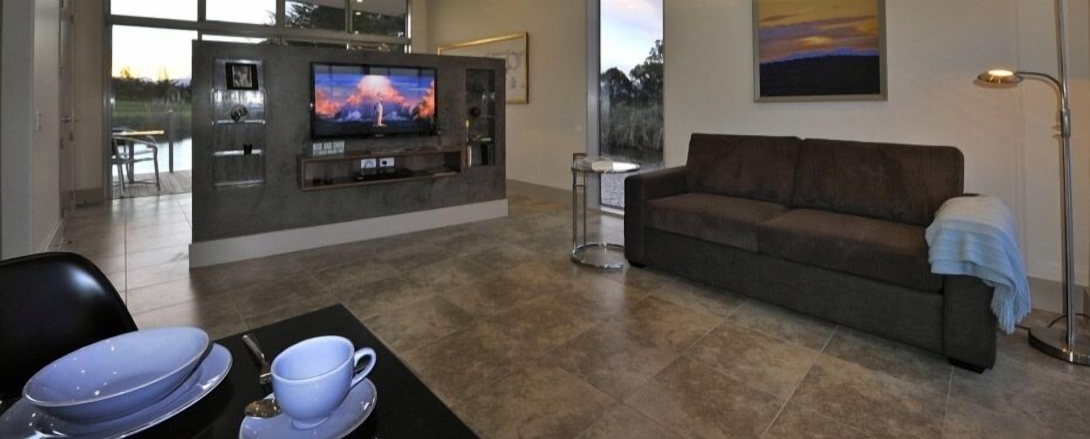 A modern living room with a flat-screen TV, a sofa, and a dining area with a table set for two.