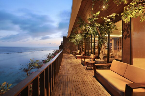 Une terrasse en bois avec un canapé et des fauteuils, donnant sur une étendue d’eau.