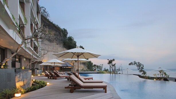 Un espace aménagé au bord de la piscine, avec des chaises longues et des parasols, donnant sur une étendue d’eau.