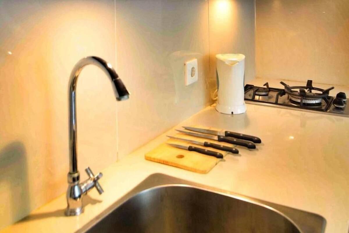 A kitchen with a stainless steel sink, a gas stove, a cutting board, and several knives.
