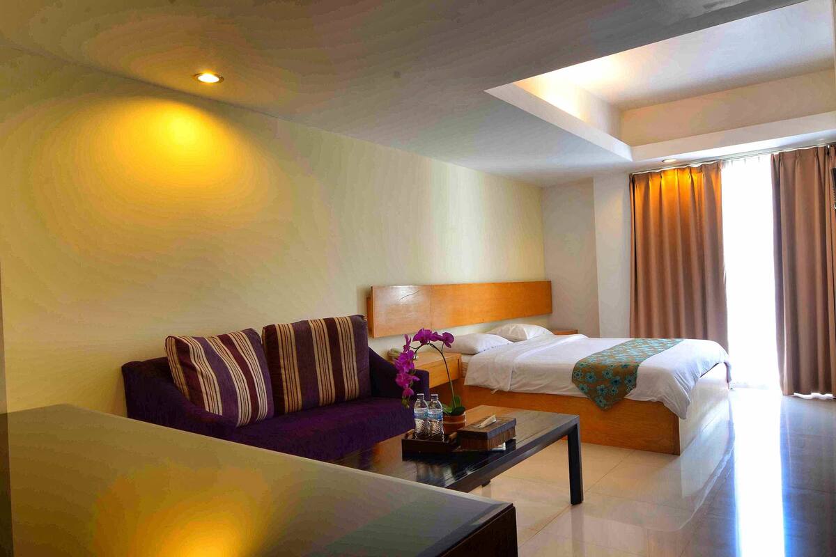 A hotel room with a bed, a sofa, a coffee table, and a small table with a vase of flowers.