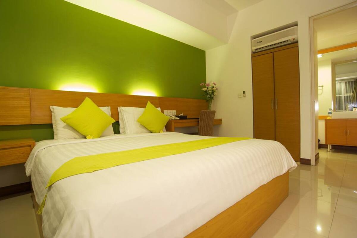 A hotel room with a large bed, a nightstand, a wooden wardrobe, and a bathroom visible through an open door.