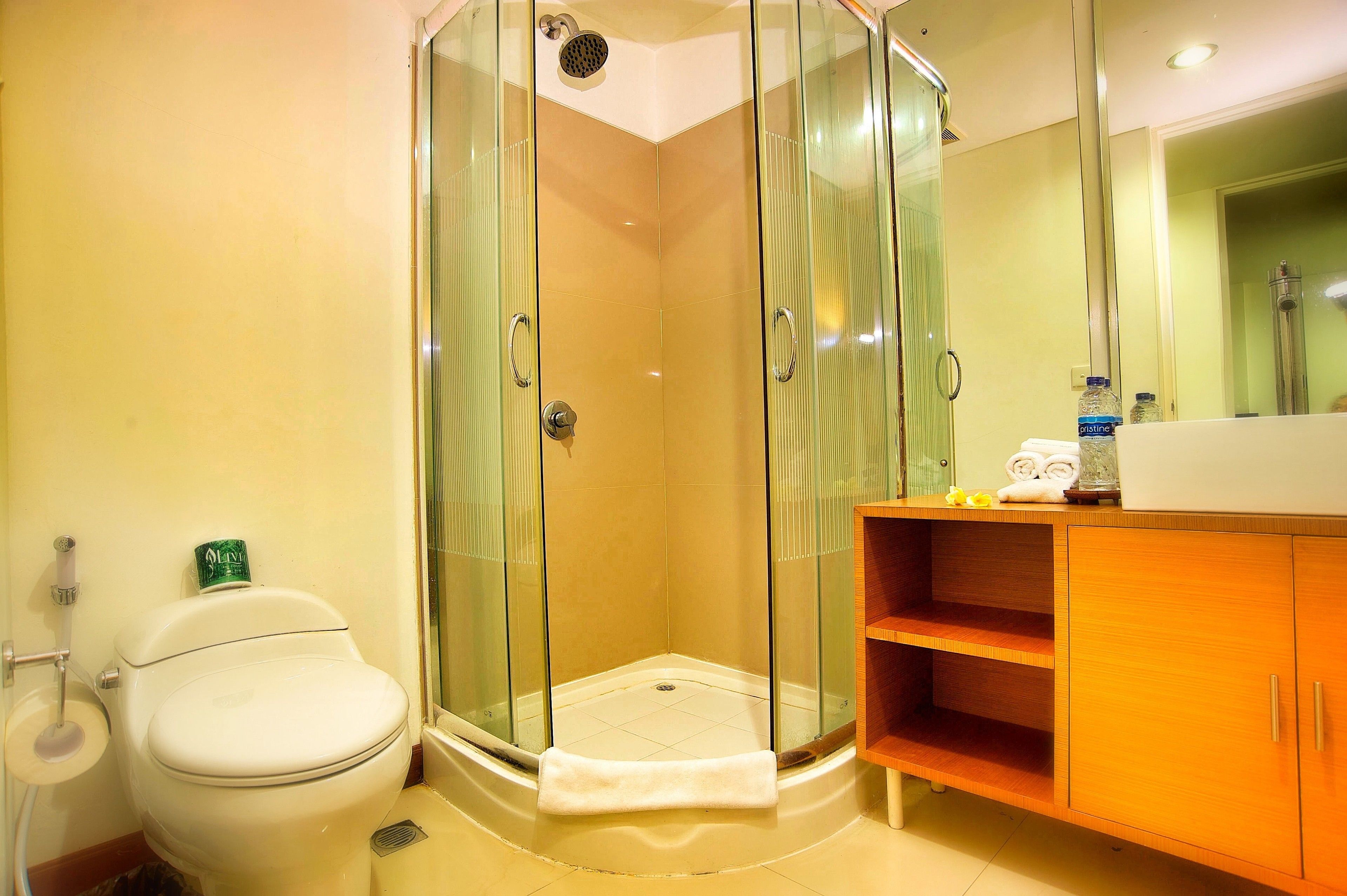 A bathroom with a glass-enclosed shower, a toilet, and a wooden vanity with a mirror.