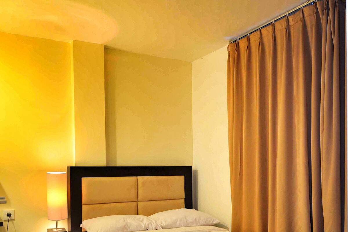A hotel room with a bed, a nightstand, a lamp, and a curtain.