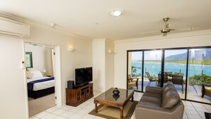 A living room with a sofa, a coffee table, and a TV. There is a balcony with a view of the ocean. - Jack & Newell Holiday Apartments (Cairns)
