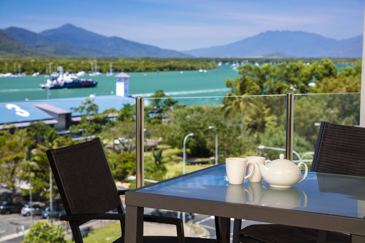 A table with a teapot and cup, overlooking a marina with boats and a mountain view.