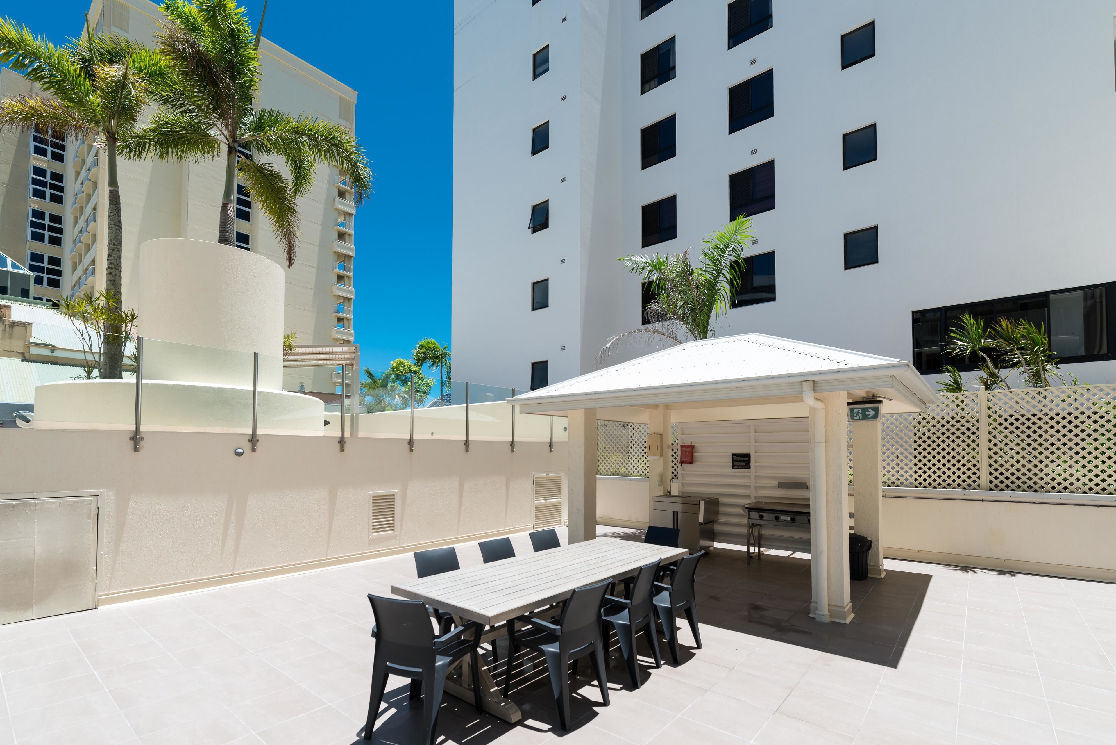Une terrasse extérieure avec une longue table et des chaises, un espace salon couvert et une vue sur un grand immeuble doté de nombreuses fenêtres.