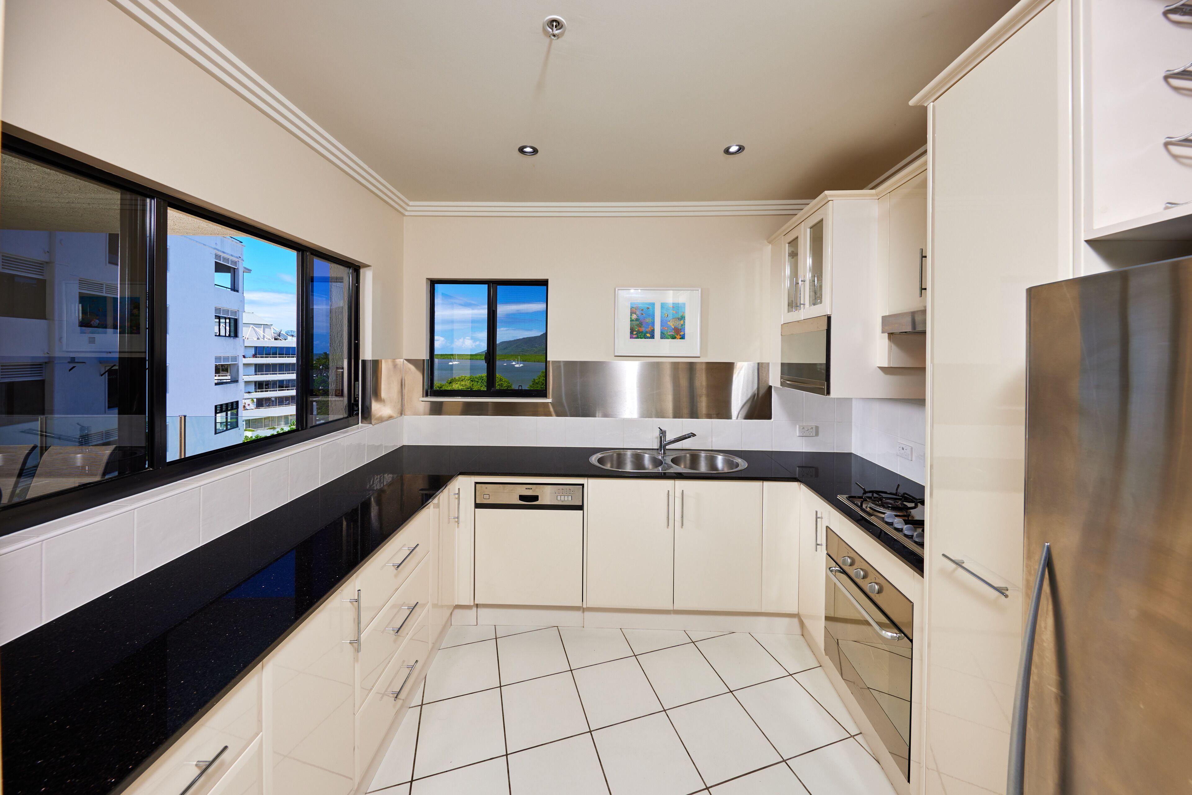 A modern kitchen with a black countertop, stainless steel appliances, and a view of a building through a large window.