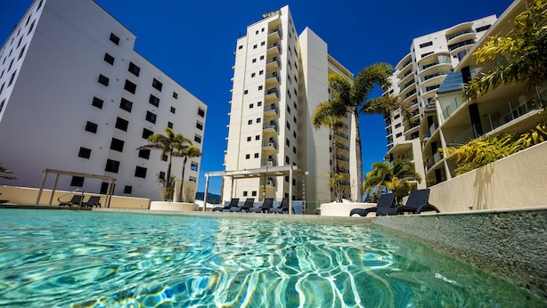 A swimming pool with clear water, surrounded by high-rise buildings and palm trees. - Jack & Newell Holiday Apartments (Cairns)