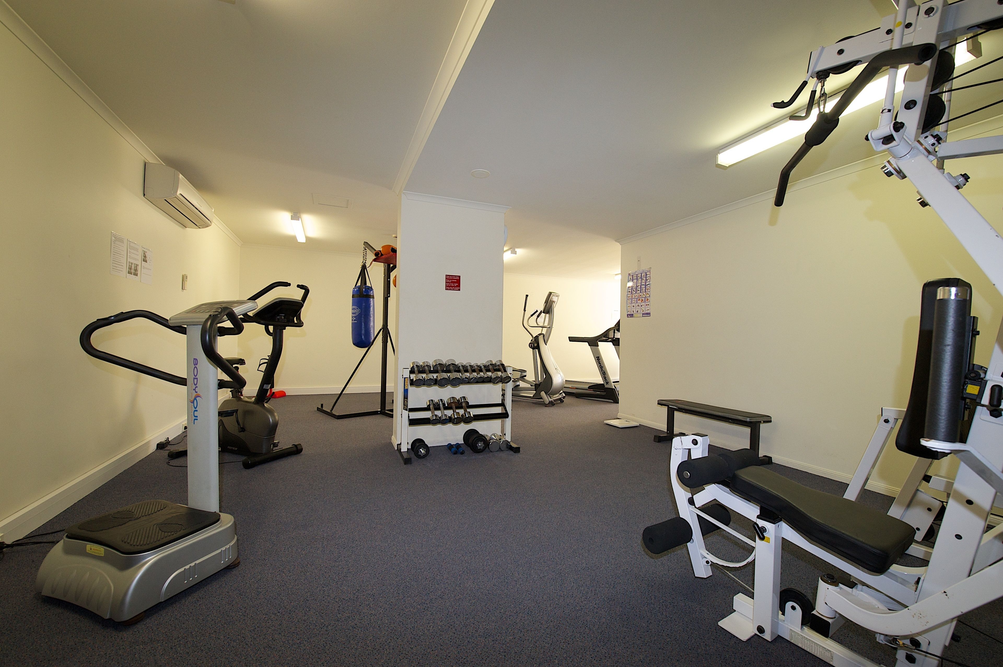 Een fitnessruimte met cardioapparaten, gewichthefapparatuur en dumbbells.