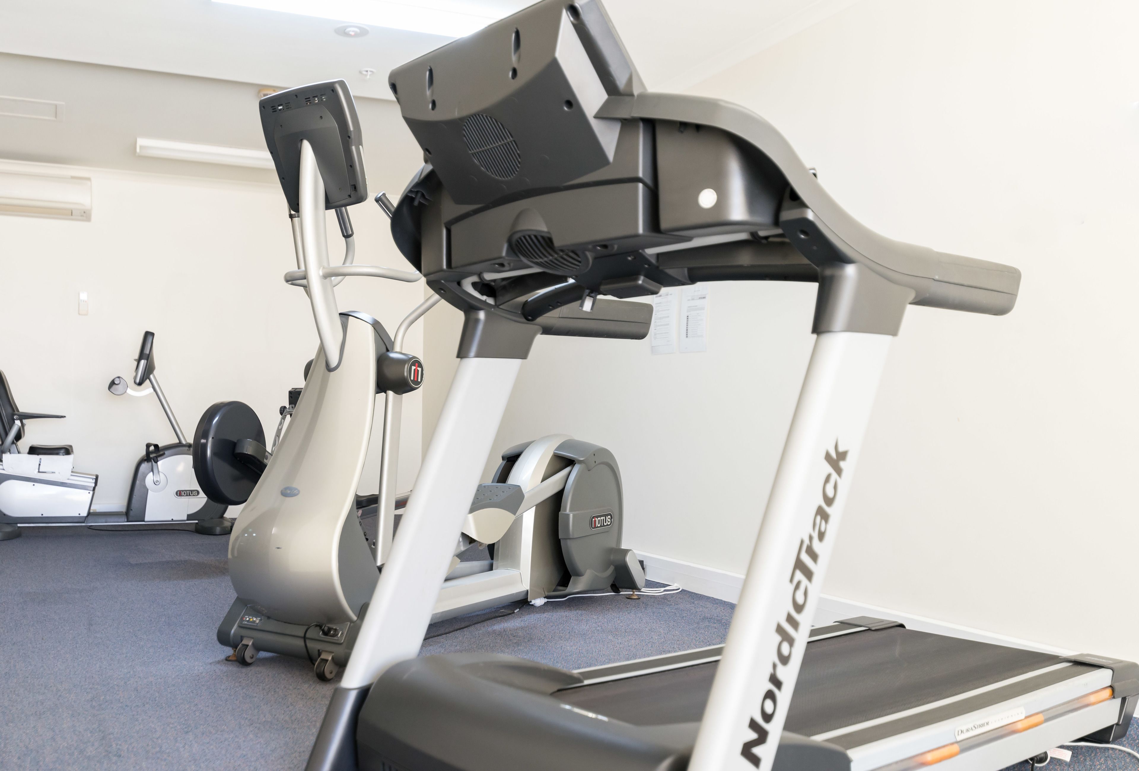 Una caminadora con el logotipo de NordicTrack, una bicicleta estática y una máquina de remo en un gimnasio.