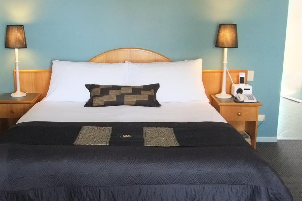 A hotel room with a bed, two bedside tables with lamps, a telephone, and a wall-mounted radio.