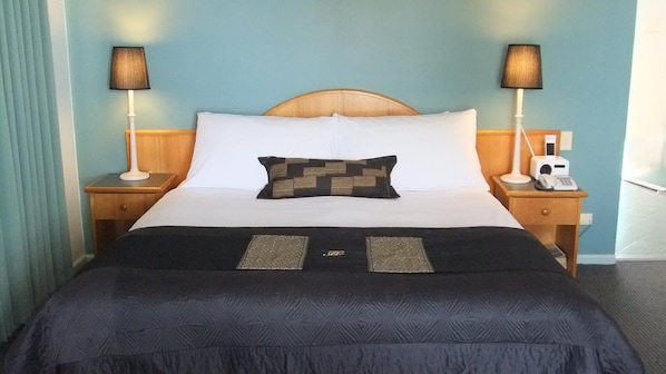 Habitación de hotel con cama, dos mesitas de noche con lámparas, teléfono y radio incorporada a la pared.