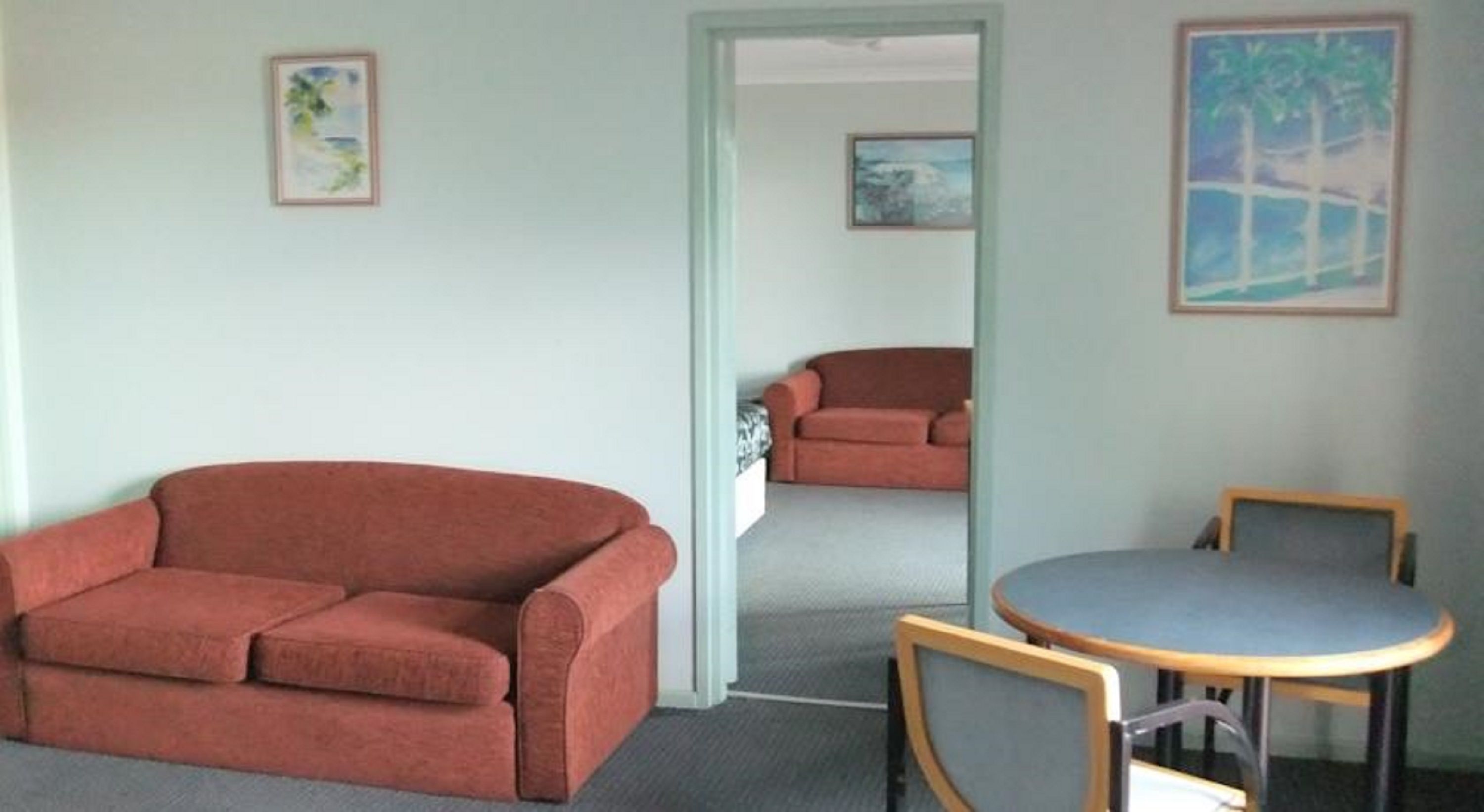 A room with a red sofa, a round table with chairs, and two paintings on the walls.