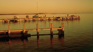 A pier extending into calm water with boats docked and a lighthouse in the distance. - Heritage Resort Shark Bay (Denham)