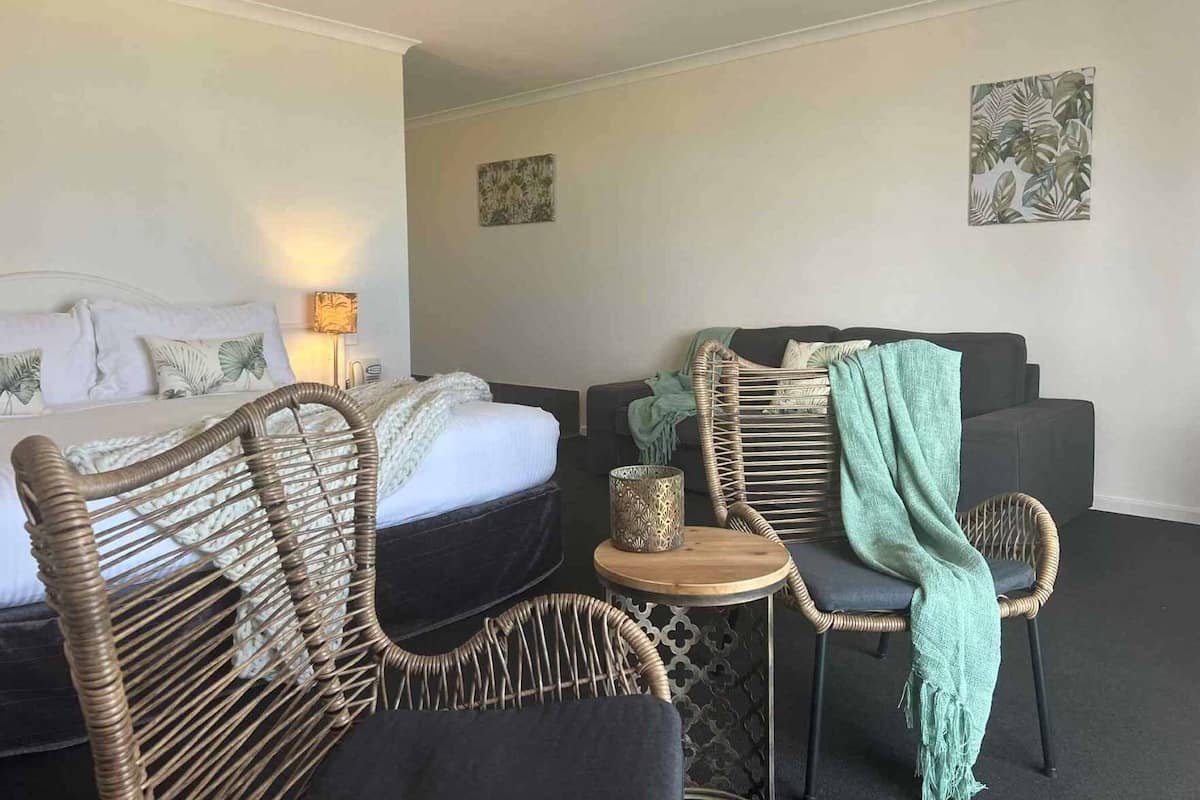 A hotel room with a bed, two wicker chairs, a small table, and a sofa.