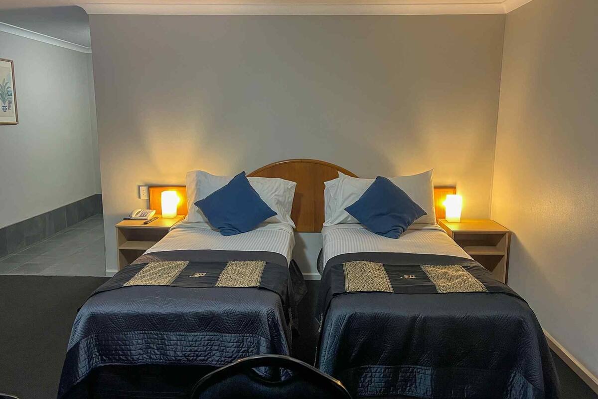 A hotel room with two single beds, each with a headboard, bedside tables, and lamps.