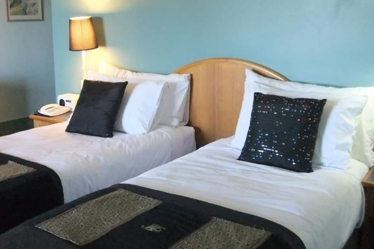 A hotel room with two beds, each with white bedding and black and white pillows. There is a lamp on the nightstand beside each bed.