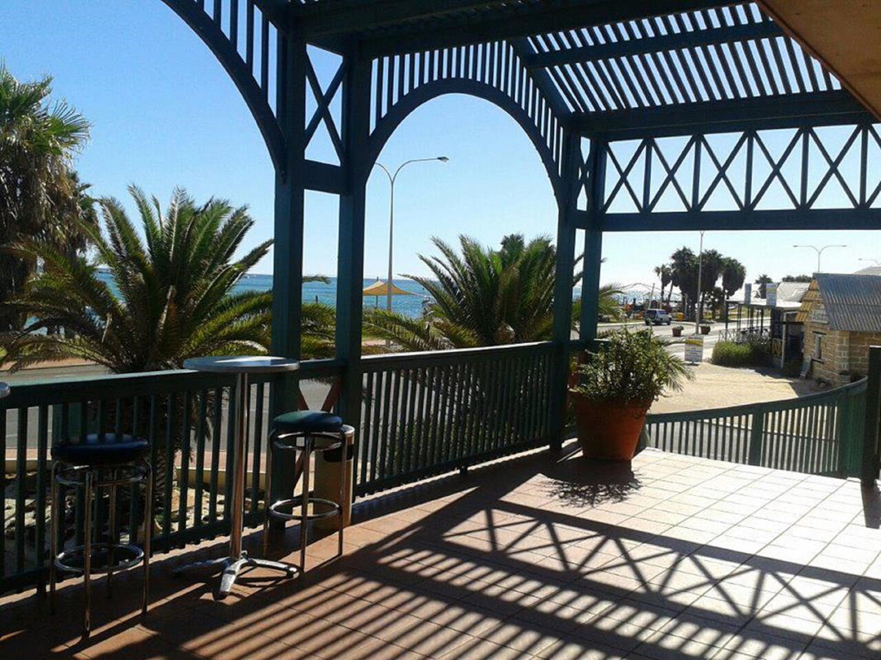 A covered outdoor area with a view of the sea, featuring a gazebo, seating, and potted plants.