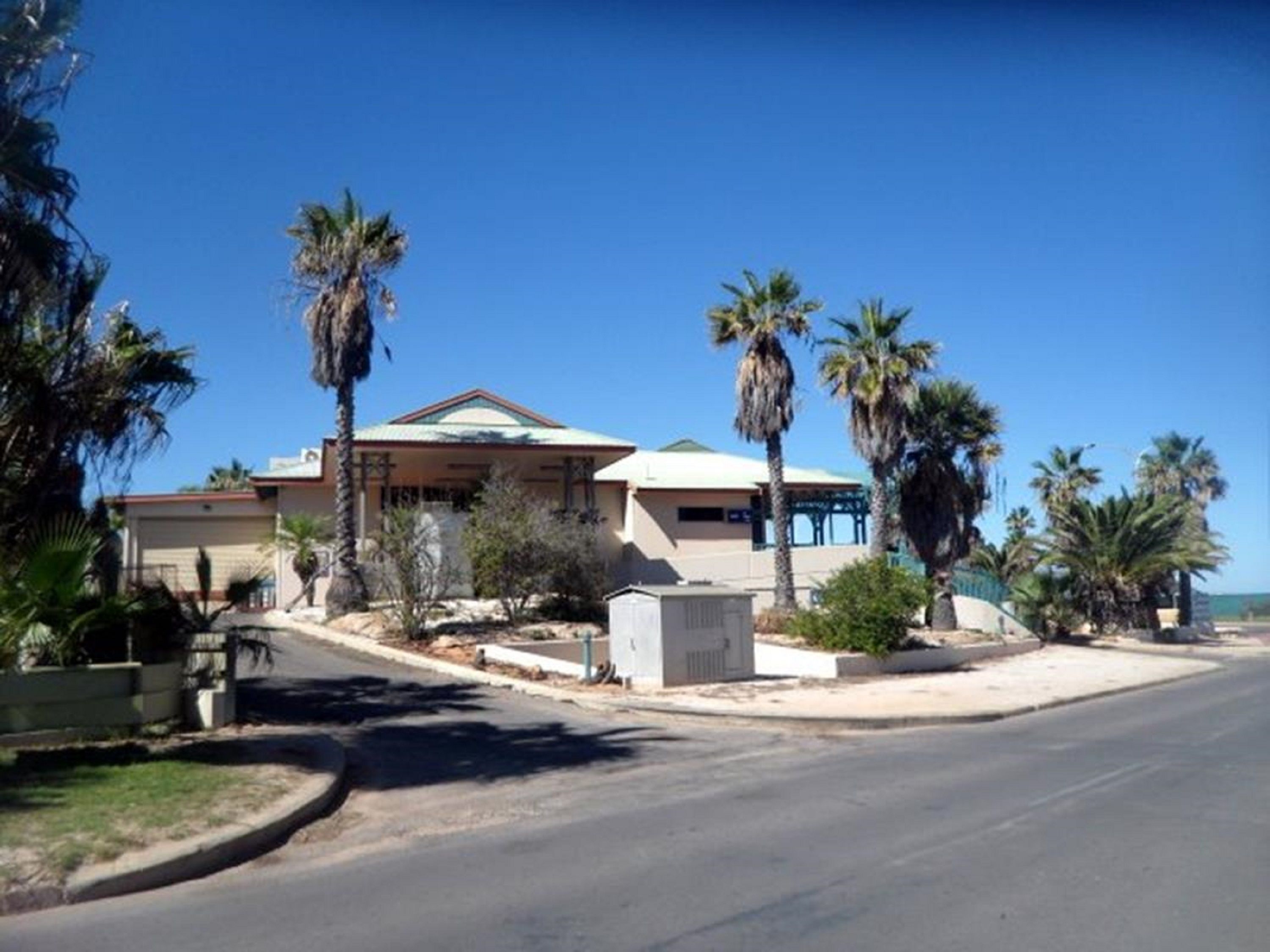 A two-story house with a flat roof, surrounded by palm trees and a clear blue sky.