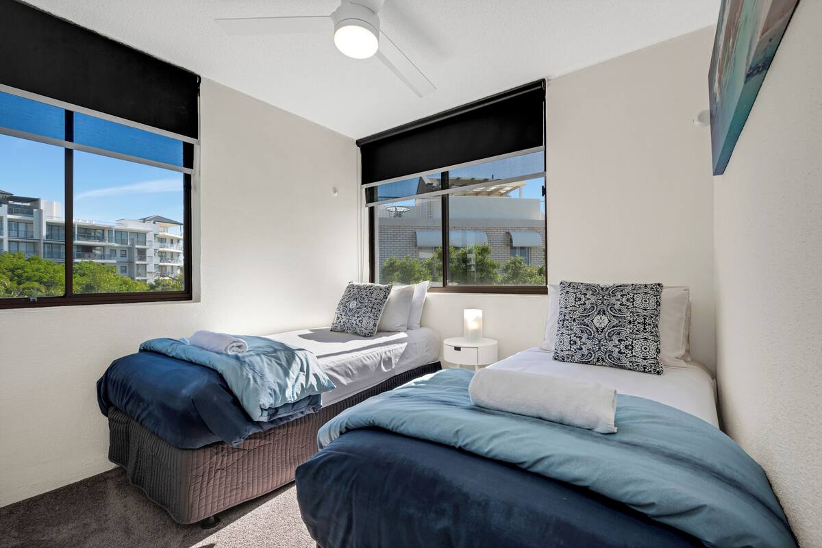 A modern bedroom with two beds, large windows, and a ceiling fan.