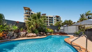 A swimming pool with a tiled edge, surrounded by palm trees and a building with balconies. - Mylos Holiday Apartments (Maroochydore)