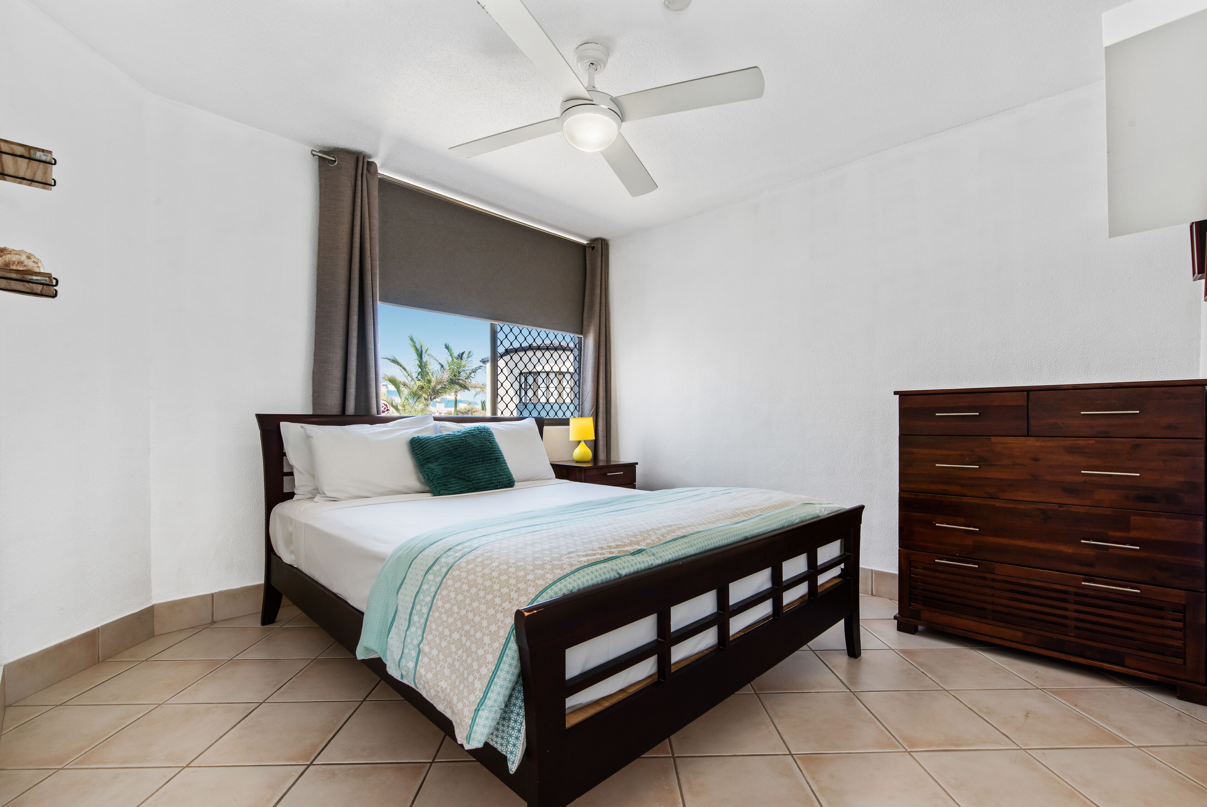A bedroom with a bed, a ceiling fan, a nightstand, a dresser, and a window with curtains.