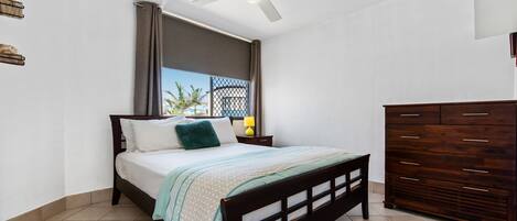 A bedroom with a bed, a ceiling fan, a nightstand, a dresser, and a window with curtains.