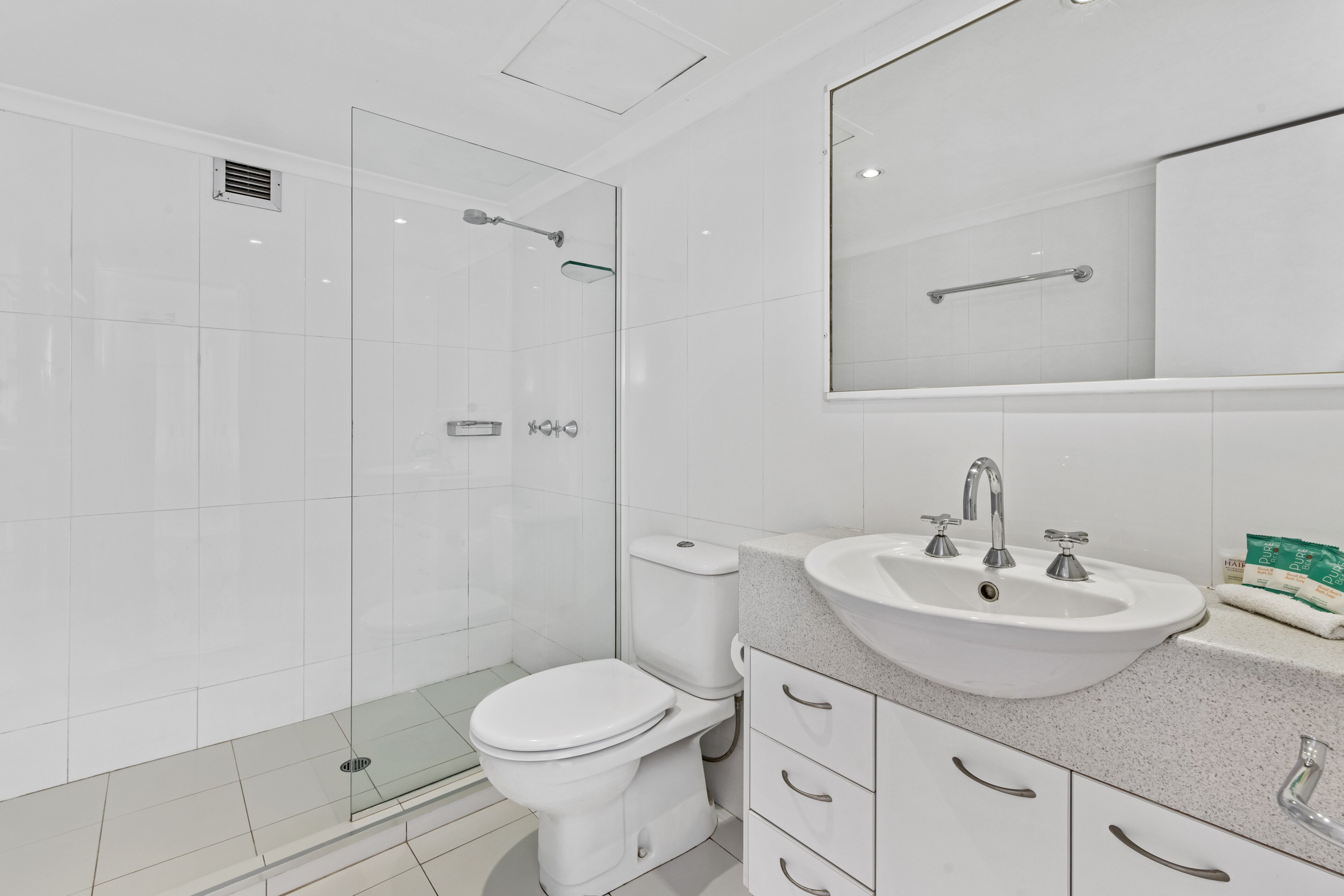 A modern bathroom with a glass-enclosed shower, a white toilet, and a sink with a mirror above.