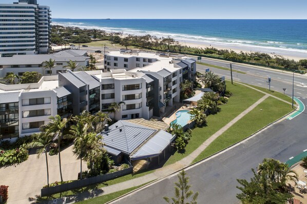 A modern hotel complex with multiple buildings, a swimming pool, and a view of the beach and ocean. - Mylos Holiday Apartments (Maroochydore)