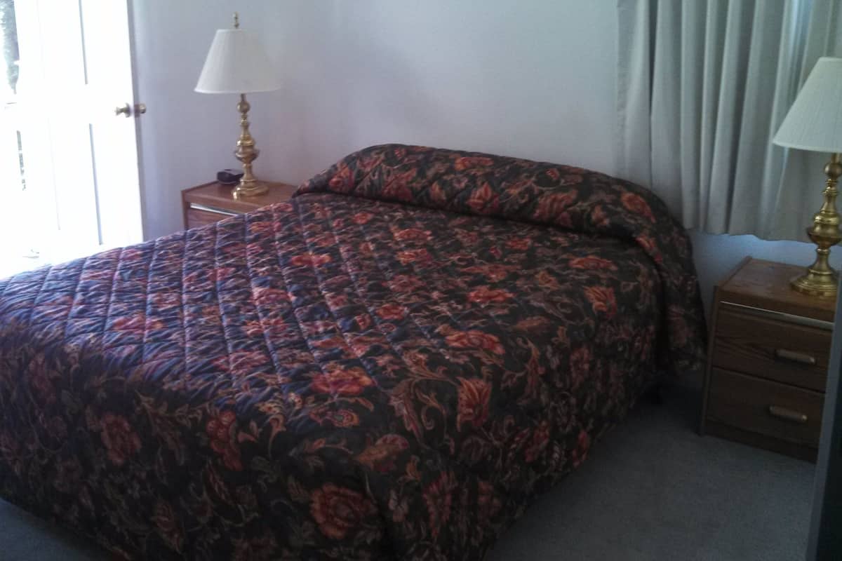 Un dormitorio con una cama, dos mesitas de noche con lámparas, una puerta y una ventana.
