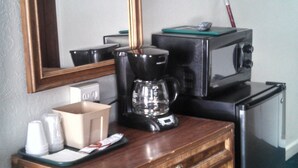 Quarto de hotel compacto com escrivaninha de madeira, cafeteira, micro-ondas e pequena geladeira.