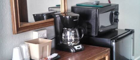 Una habitación de hotel compacta con un escritorio de madera, cafetera, microondas y un refrigerador pequeño.