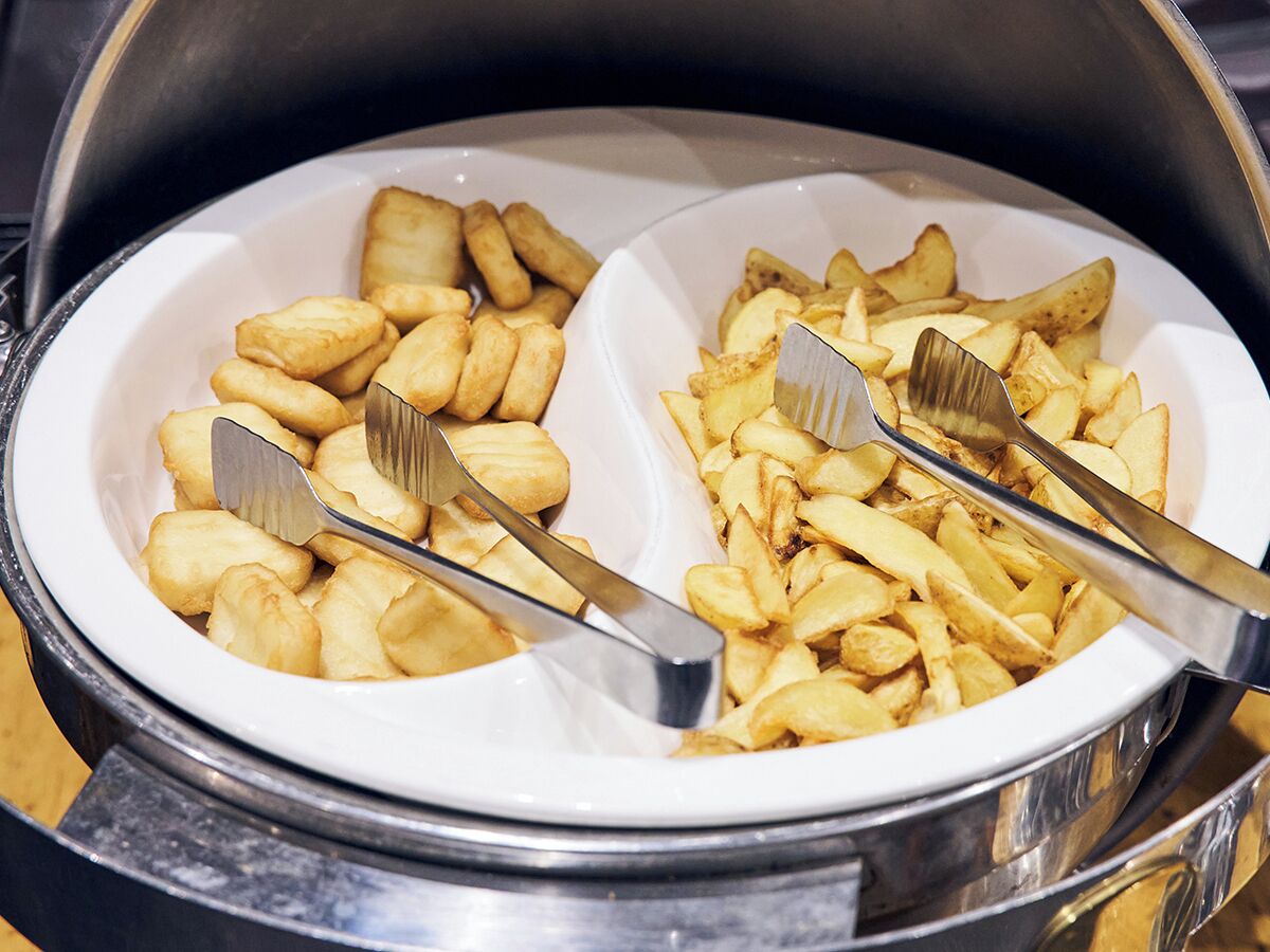 Un bufé con dos platos blancos que contienen papas fritas y wedges de papa, cada uno con un par de pinzas.