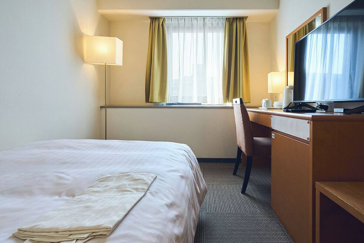 A hotel room with a bed, a desk, a chair, a television, and a window with curtains.