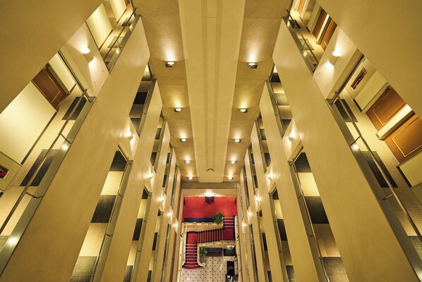 A multi-level hotel interior with a central staircase, multiple floors, and a red accent wall.