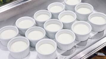 A tray of white ramekins with a creamy substance, likely custard or pudding, arranged neatly on a metallic surface.