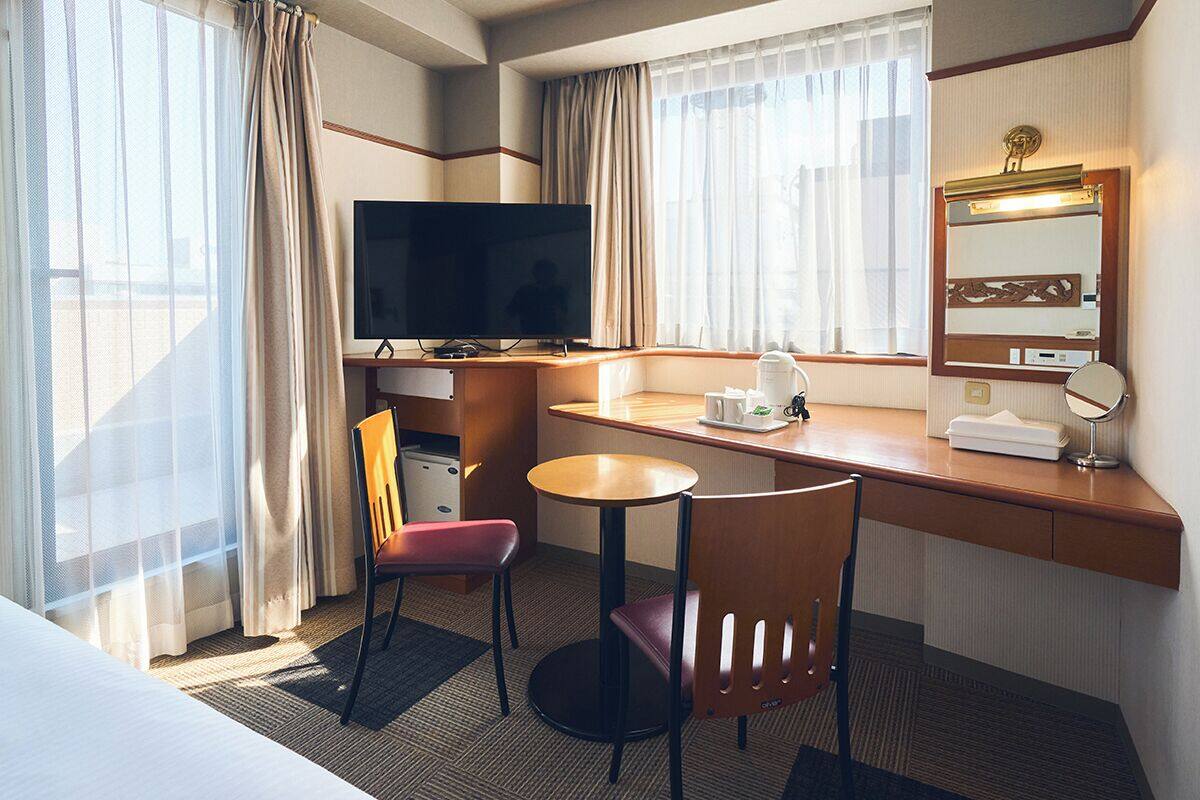 A hotel room with a bed, a desk with a computer, a TV, a chair, and a small table with a coffee maker.