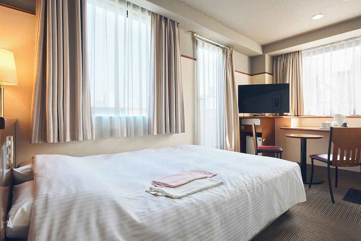 A hotel room with a large bed, a desk with a chair, a television, and curtains.